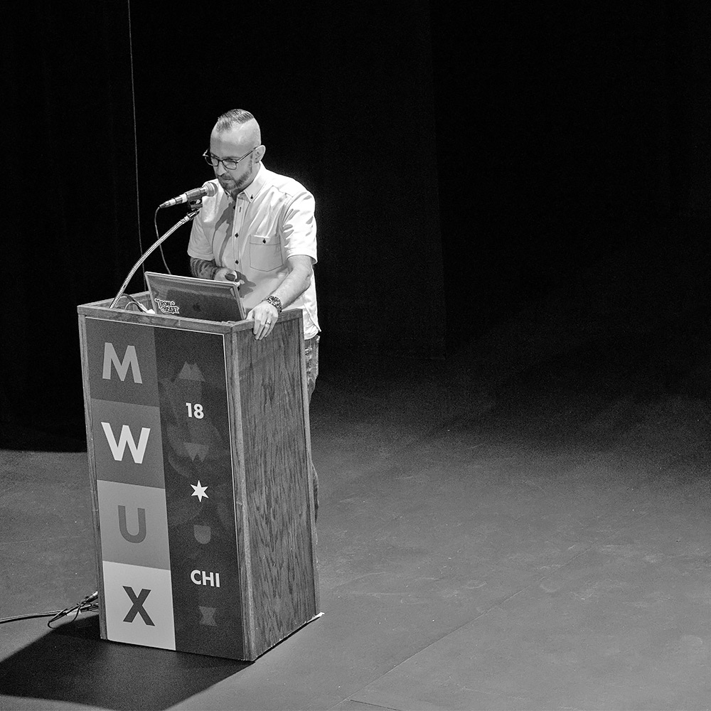 Justin standing at the podium while giving the MidwestUX opening keynote presentation